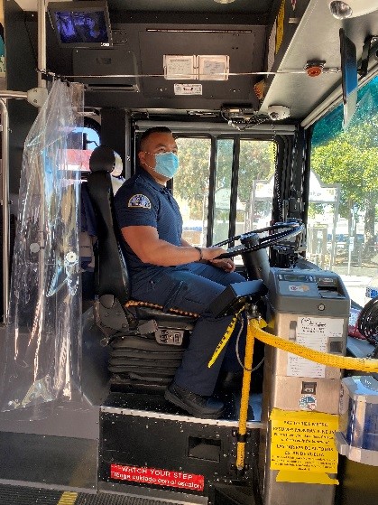 Bus operator wearing mask with plastic curtains available as a barrier between operator and passengers
